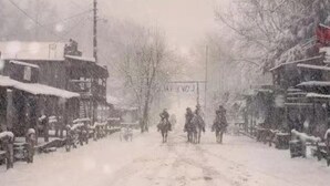 Una calle nevada con edificios a ambos lados y un cartel a lo lejos.