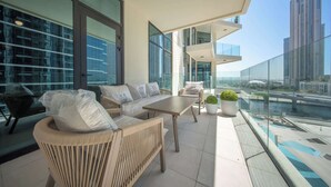 Un balcon moderne, doté d’un canapé, d’une table et de chaises, offrant une vue sur le paysage urbain et l’étendue d’eau.