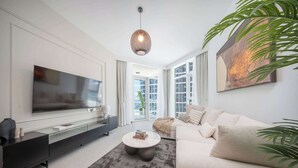 Un salon moderne doté d’un téléviseur à écran plat, d’un meuble de rangement noir, d’une table basse ronde, d’un canapé beige et d’une grande fenêtre avec des rideaux.