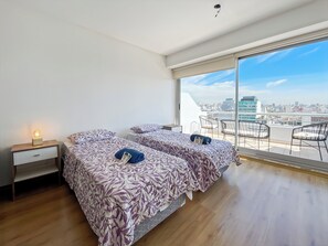 Een moderne slaapkamer met twee bedden, een nachtkastje en een groot raam met uitzicht op de stad.
