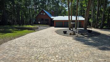 A brick pathway leading to a wooden cabin with a red roof, surrounded by a forested area.