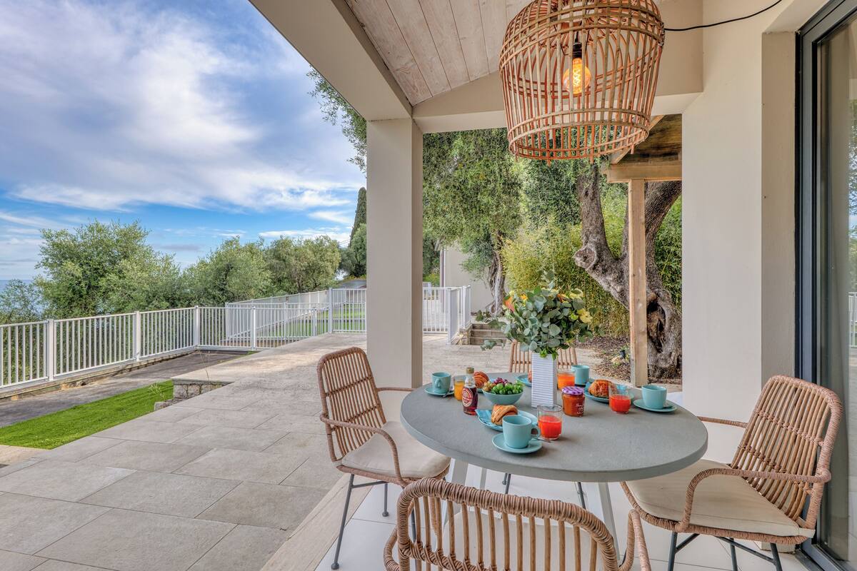 Une terrasse avec des chaises en osier, une table ronde ornée d’un vase de fleurs et un luminaire suspendu en osier.