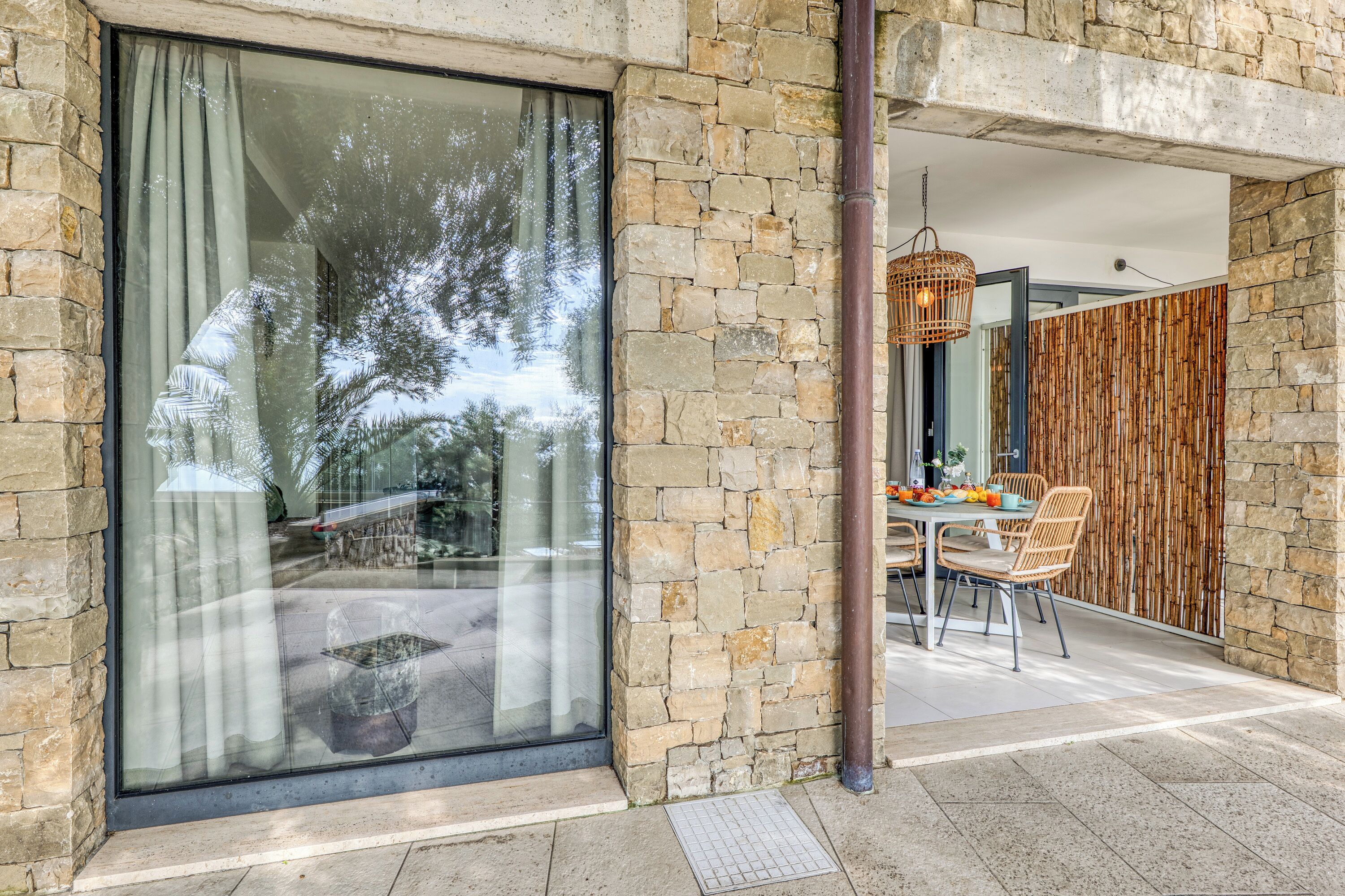 A modern outdoor dining area with stone walls, a glass window, and a bamboo wall.