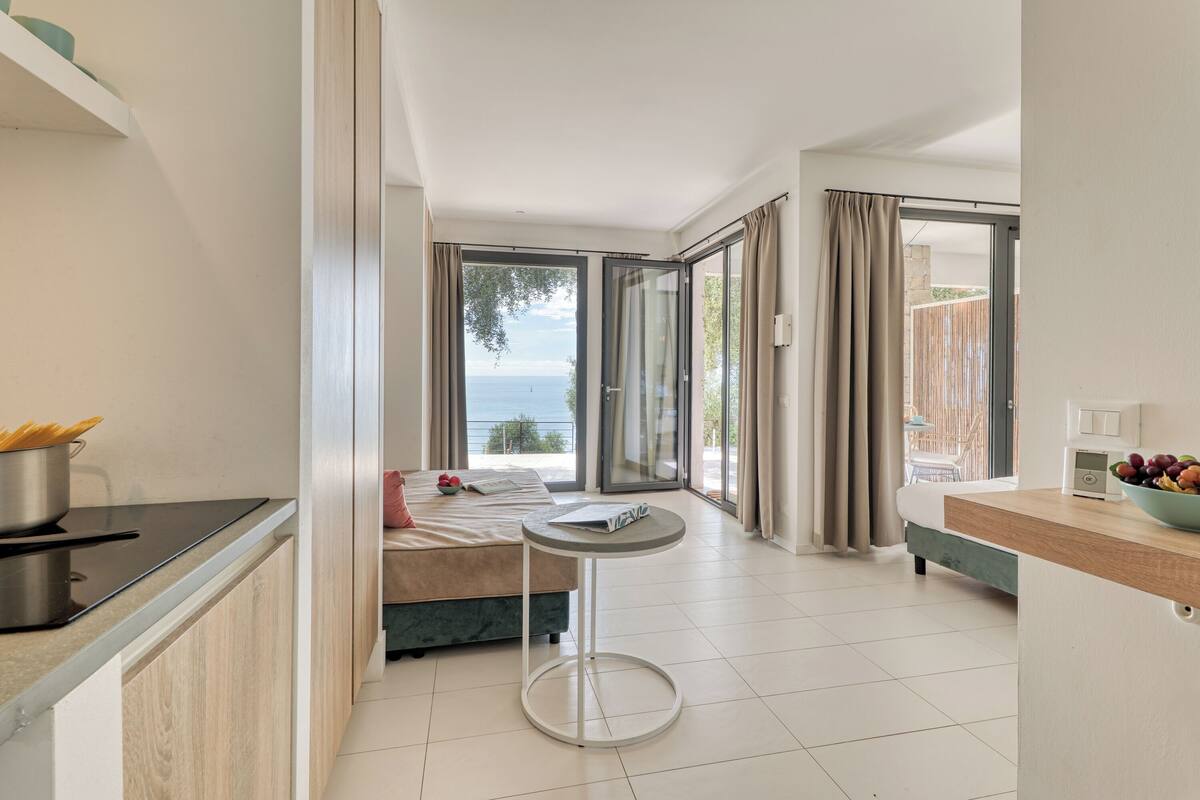 Une chambre d’hôtel moderne dotée d’un coin cuisine, d’une table à manger et d’un lit offrant une vue sur la mer.