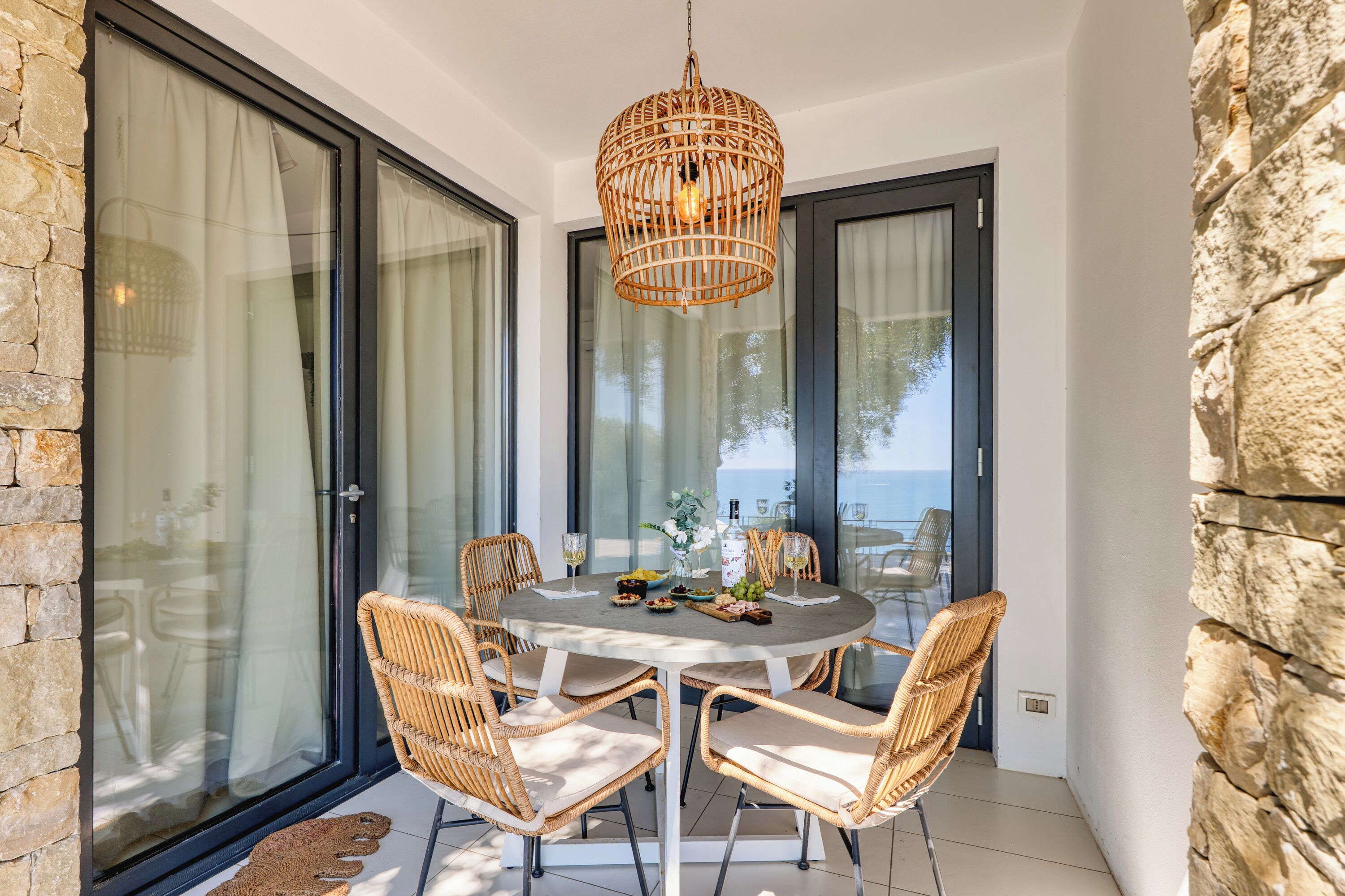A dining area with a round table, wicker chairs, and a hanging light fixture.