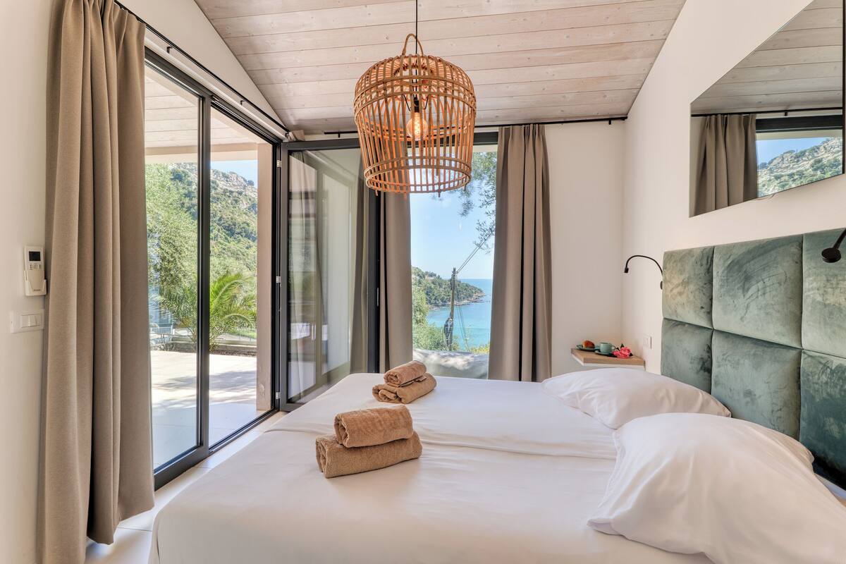 Une chambre d’hôtel moderne avec un grand lit, une vue sur la mer et un plafond en bois.