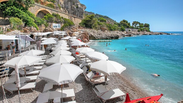 A beach with white umbrellas and lounge chairs, a rocky coastline, and a clear blue sea. - Holiday Resort Balzi Rossi (Ventimiglia)