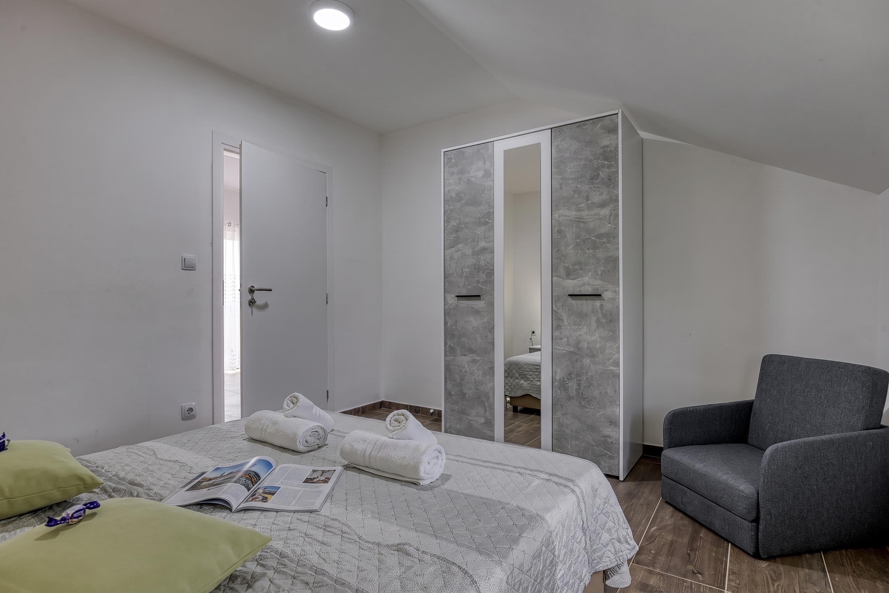 A modern bedroom with a bed, a grey armchair, and a walk-in closet.