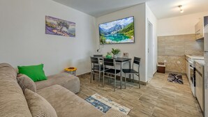 Una sala de estar moderna con un sofá, una mesa de comedor con sillas, un televisor y una zona de cocina con estufa.