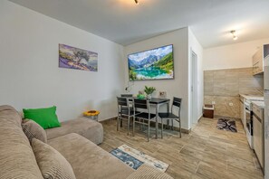A modern living room with a sofa, a dining table with chairs, a TV, and a kitchen area with a stove. - Island Top Sea View Estate (Mali Losinj)