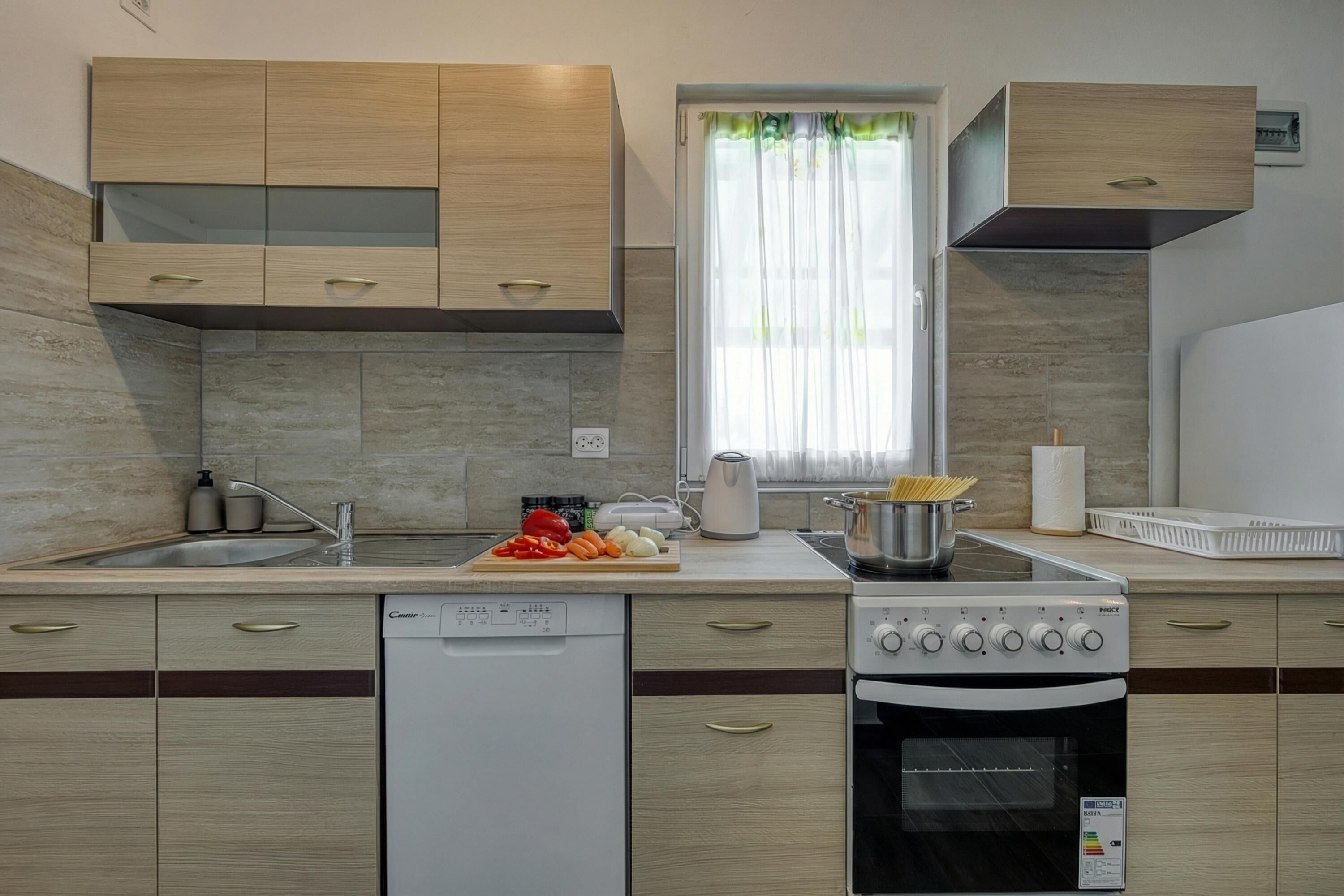 A modern kitchen with a dishwasher, stove, oven, and a window with curtains.