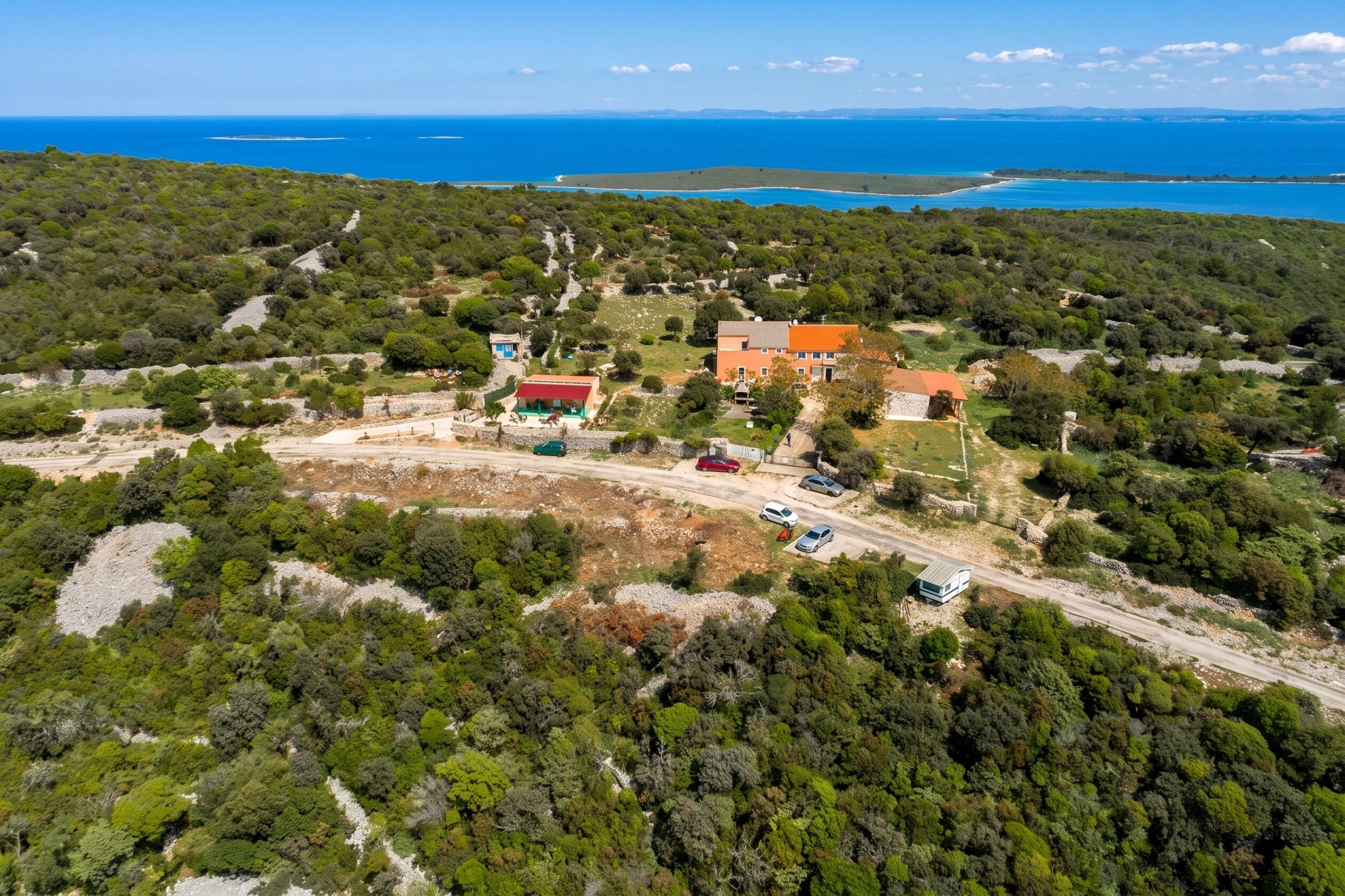 Vue aérienne d’une propriété située sur la côte, comprenant un bâtiment principal, un espace de stationnement et une route menant à la mer.