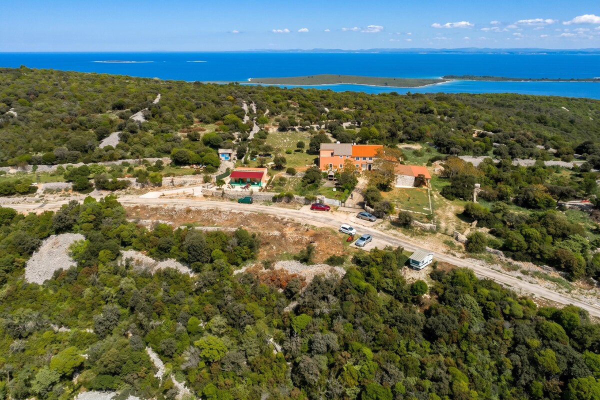 An aerial view of a coastal property with a main building, a parking area, and a road leading to the sea.