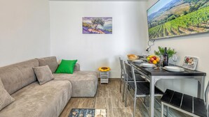 Una sala de estar con un sofá, una mesa de comedor para dos personas, una mesita auxiliar y un cuadro en la pared.