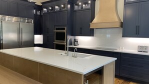 Una cocina moderna con armarios oscuros, electrodomésticos de acero inoxidable, una isla grande con fregadero y piso de madera.