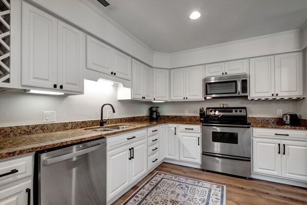 A modern kitchen with white cabinetry, stainless steel appliances, granite countertops, and a patterned rug.