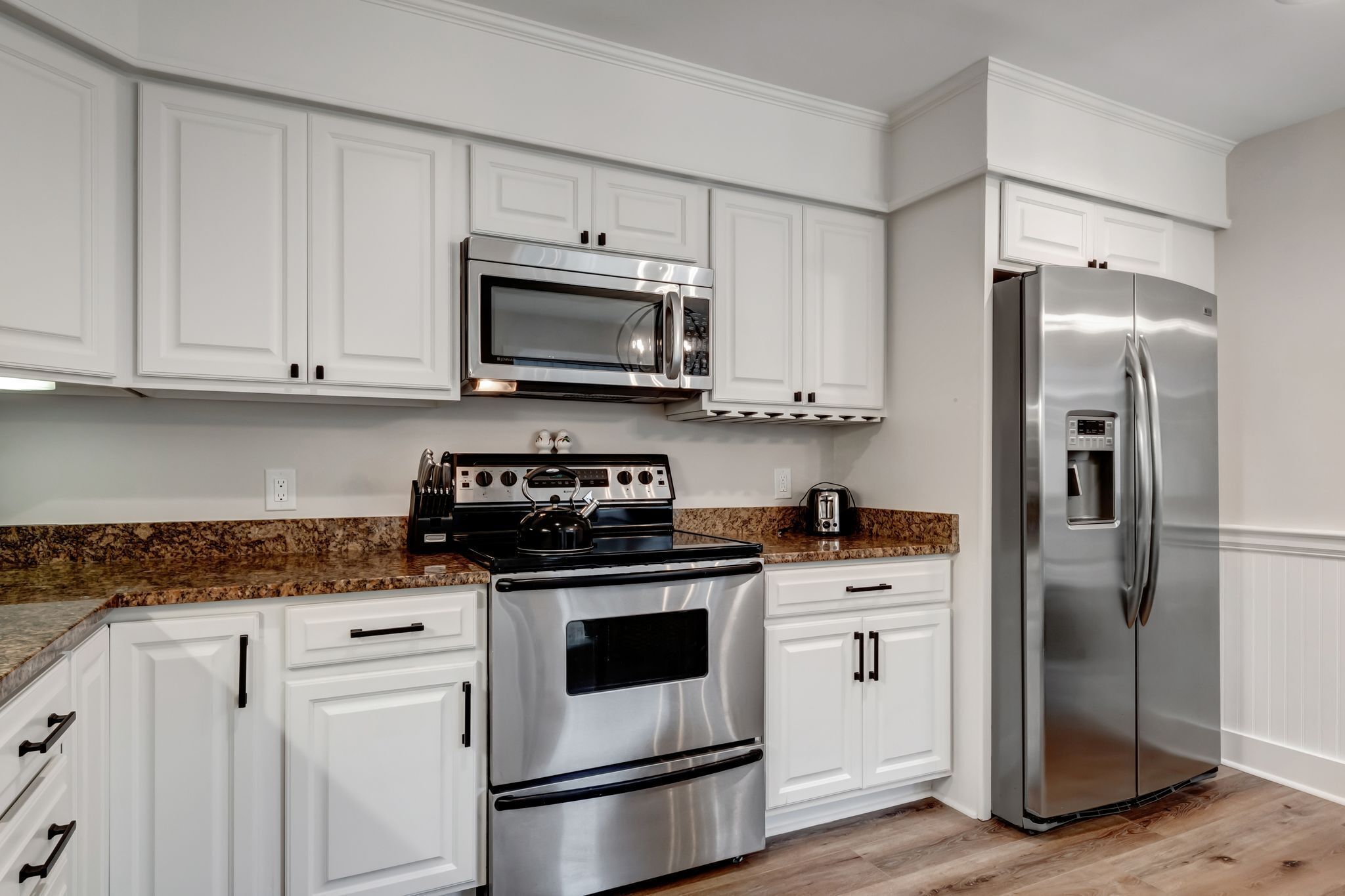 Una cocina con armarios blancos, horno de acero inoxidable, microondas y refrigerador.