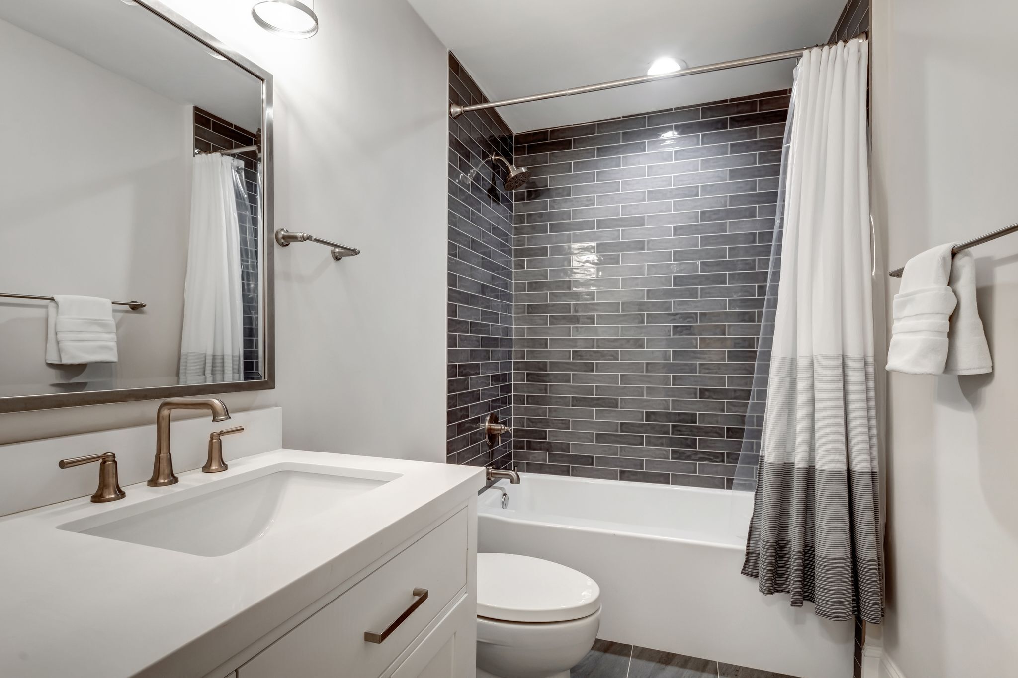 A modern bathroom with a white sink, two gold faucets, a white toilet, and a bathtub.