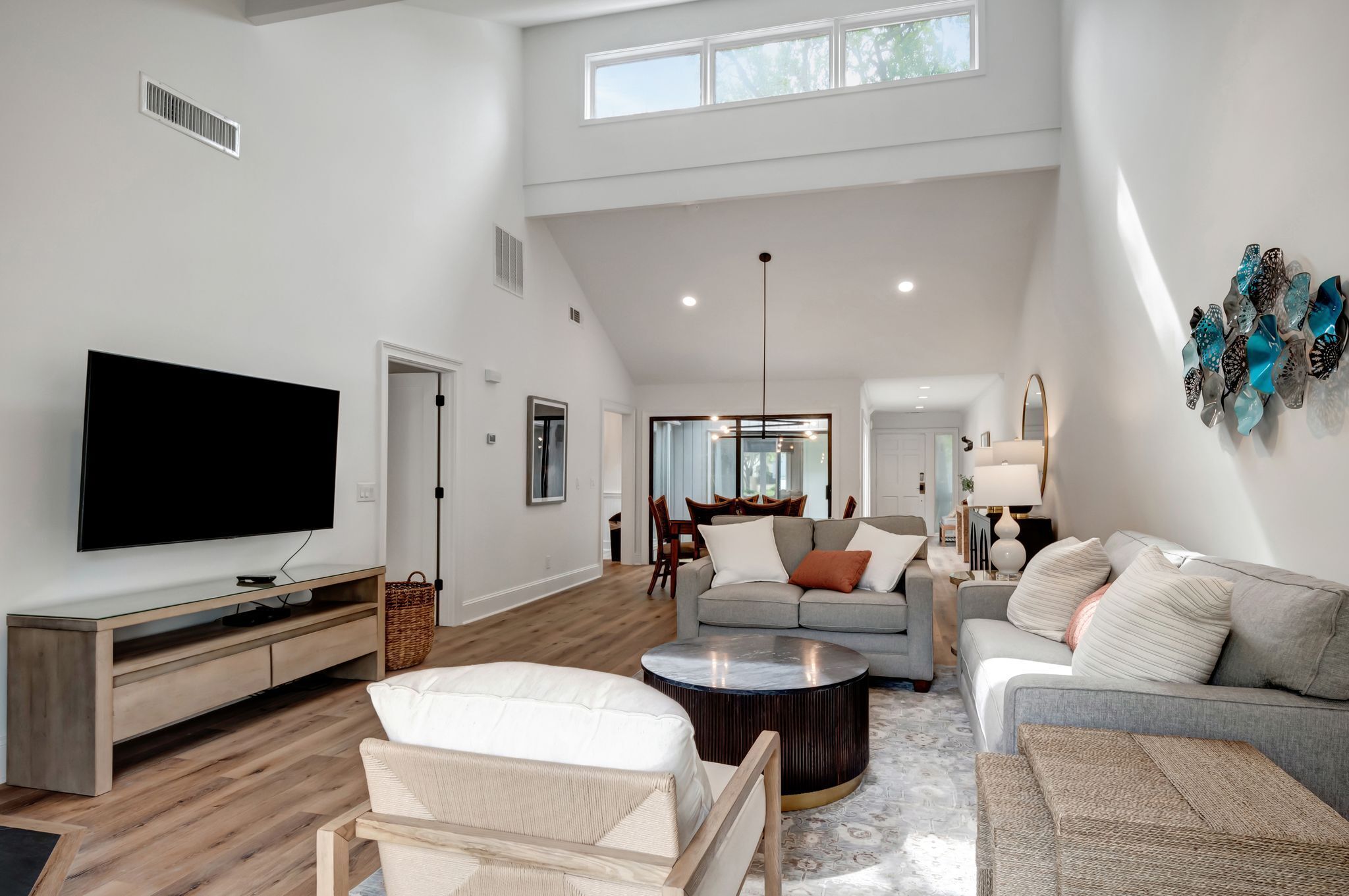 A spacious living room with a flat-screen TV, a sofa, a coffee table, and a dining area in the background.