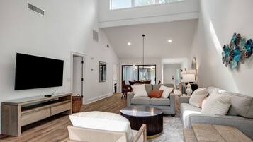 A spacious living room with a flat-screen TV, a sofa, a coffee table, and a dining area in the background.