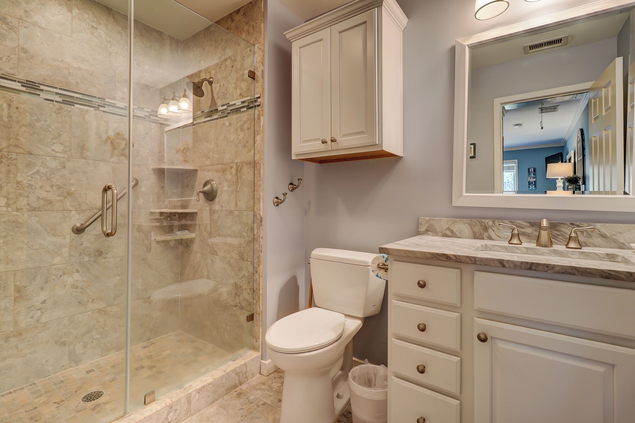 A bathroom with a glass-enclosed shower, a toilet, and a vanity with a mirror.