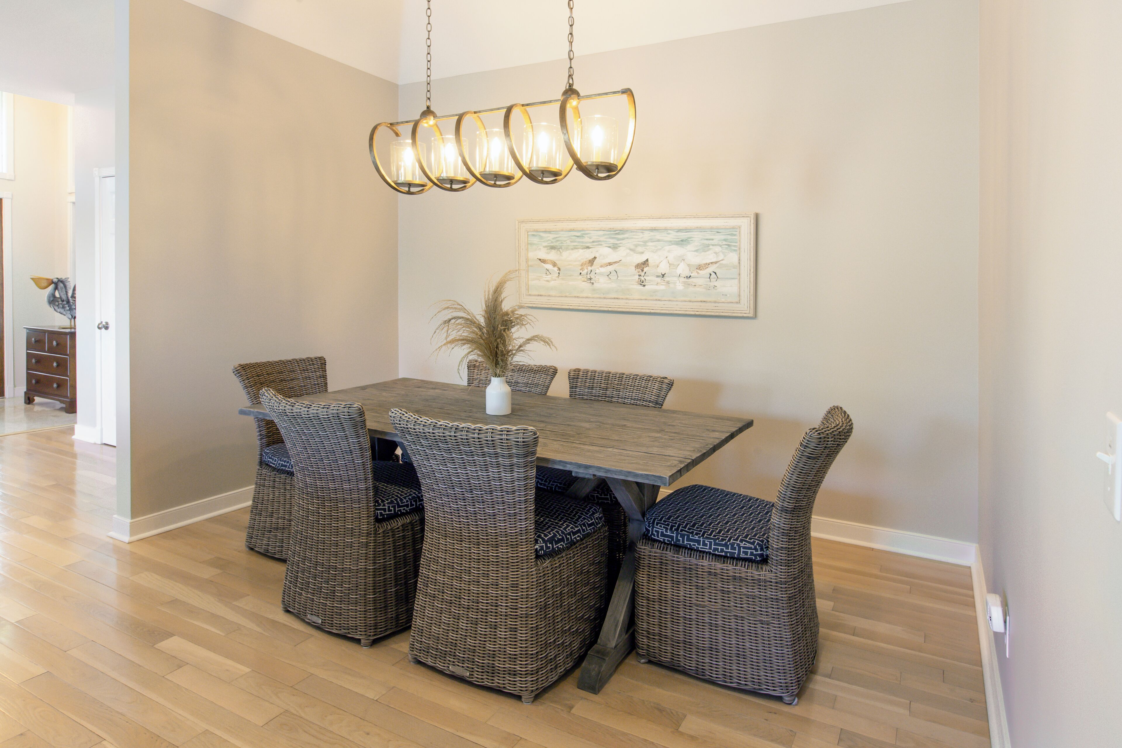 Un coin repas avec une table en bois et des chaises en osier, un luminaire suspendu et un tableau encadré au mur.