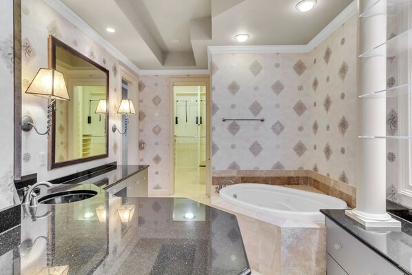 A modern bathroom with a large mirror, two wall-mounted lights, a black sink, a bathtub, and a vanity with a mirror.