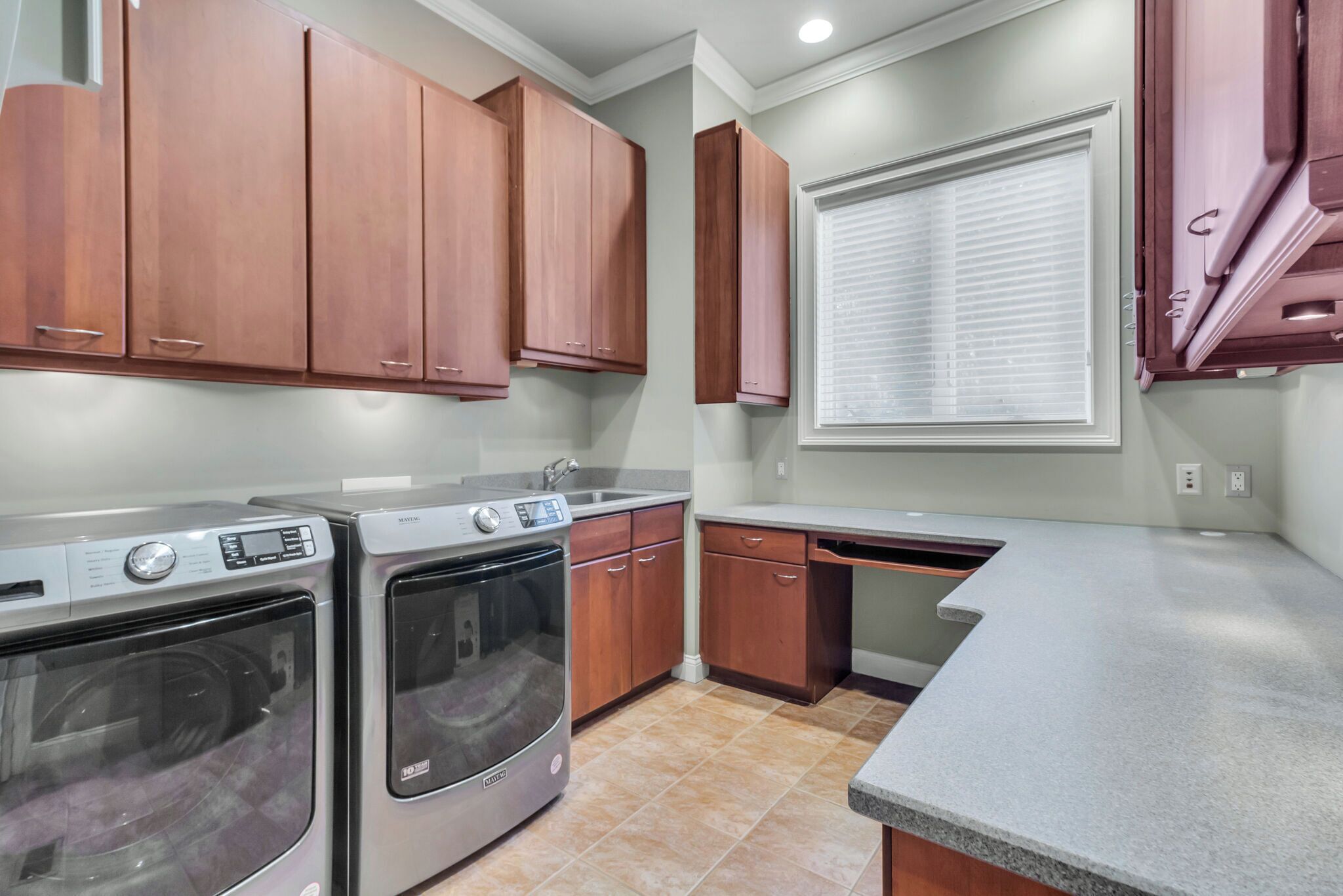 A kitchen with built-in appliances, wooden cabinets, and a window with blinds.