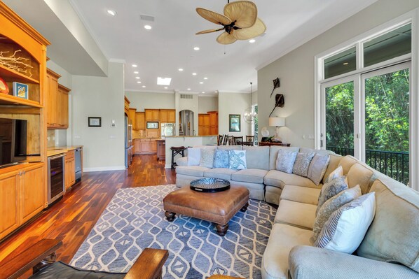 A spacious living room with a large sectional sofa, a wooden entertainment center, and a kitchen in the background.