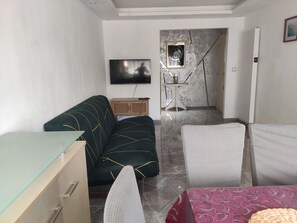 A living room with a sofa, a TV, a small table, and a patterned bed.