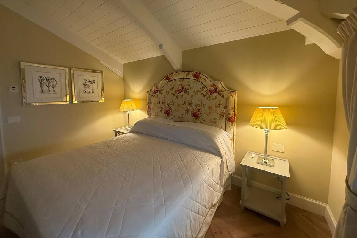 A bedroom with a large bed, two bedside tables with lamps, and two framed pictures on the wall.