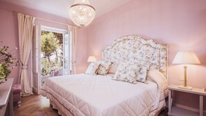 Camera da letto con un letto grande, due lampade ai comodini, un lampadario e vista sull'esterno.