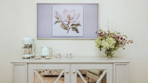 Un mobile bianco con decoro floreale, un quadro con soggetti floreali, una macchina per il caffè, tazze e un vaso con fiori.
