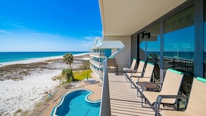 Un balcon avec vue sur la plage et l’océan, des chaises longues et une piscine.