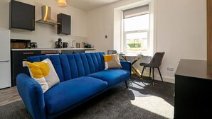Un apartamento moderno con un sofá azul, una mesa de comedor y una zona de cocina.