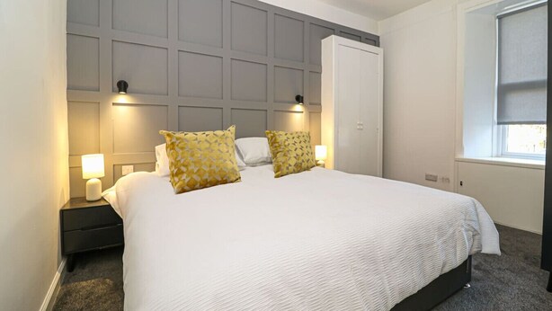 Una cama bien hecha con edredón blanco, dos almohadas decorativas y un cabecero gris.
