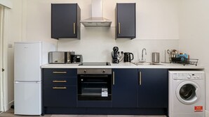 Cocina compacta con armarios oscuros, horno empotrado, lavadora y cafetera.