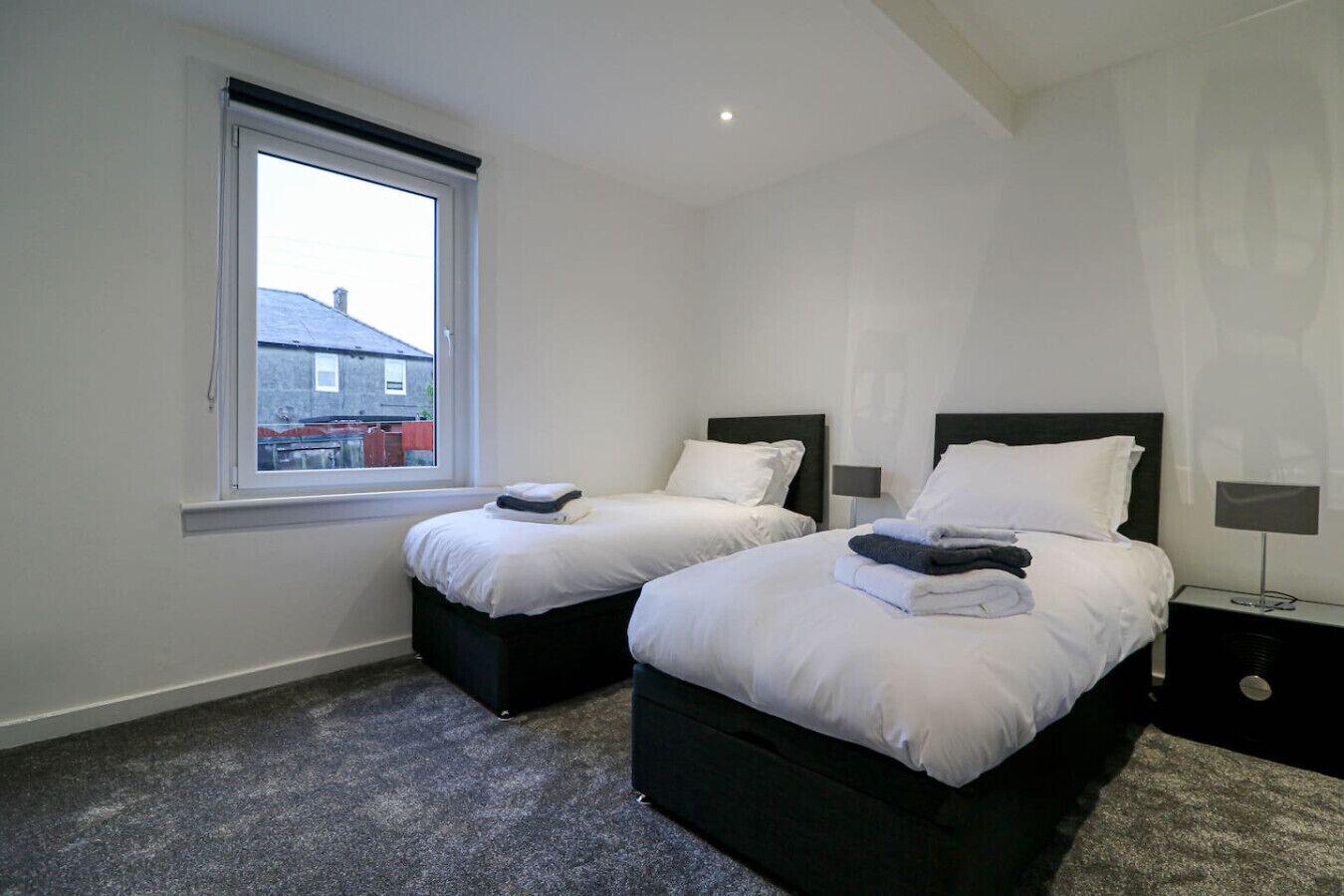A hotel room with two beds, a window, and a nightstand with a lamp.