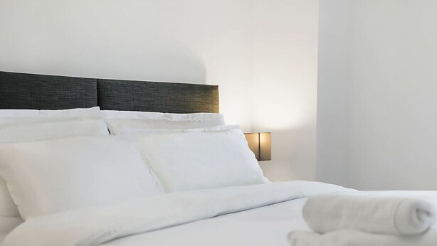 Una cama bien hecha con sábanas blancas y un cabecero oscuro.