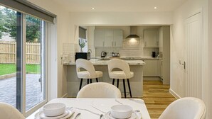 A modern kitchen with white cabinets, a marble countertop, and a dining area with white chairs and a table set for two. - Beautiful 3 Bed Luxury House in Glasgow West End (Glasgow City)