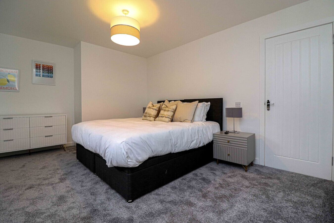A bedroom with a bed, bedside table, nightstand, and a door.