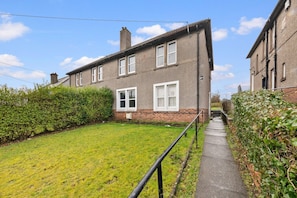 A two-story residential building with a small front yard and a pathway leading to the entrance. - Cozy 2 bed apartment in quaint countryside (Lesmahagow)