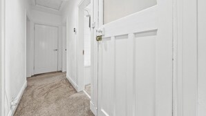 A narrow hallway with white walls and doors, carpeted flooring, and a visible electrical outlet on the wall. - Cozy 2 bed apartment in quaint countryside (Lesmahagow)
