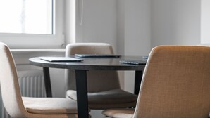 A round table with a dark surface and black legs, surrounded by two beige chairs with a textured fabric. - Cozy 2 bed apartment in quaint countryside (Lesmahagow)