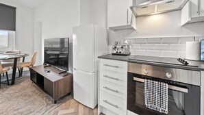 A modern kitchen with white cabinetry, a built-in oven, a toaster, and a flat-screen TV. - Cozy 2 bed apartment in quaint countryside (Lesmahagow)