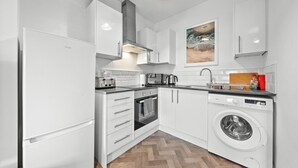 A modern kitchen with white cabinetry, a built-in oven, a washing machine, and a coffee maker. - Cozy 2 bed apartment in quaint countryside (Lesmahagow)