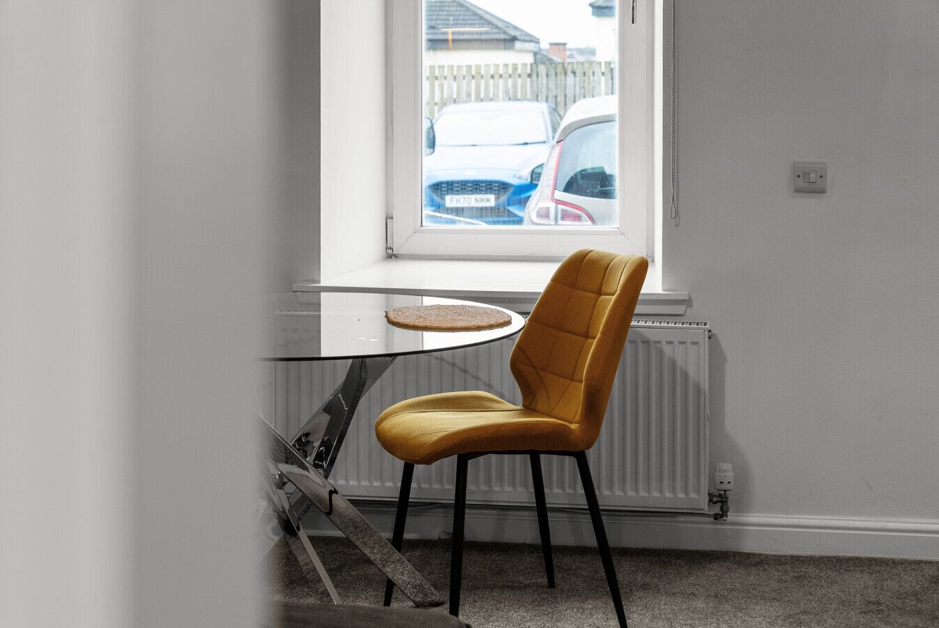 Ein Zimmer mit Fenster, einem runden Tisch und einem senffarbenen Stuhl.