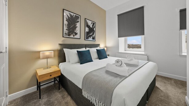 A hotel room with a bed, a nightstand, a window with a view, and two abstract paintings on the wall.