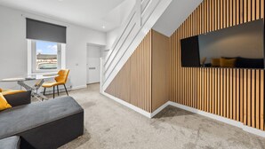 A modern interior with a staircase, a dining area with a table and chairs, and a seating area with a sofa and ottoman.