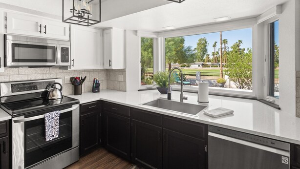 A modern kitchen with a large window, stainless steel appliances, and black cabinets.